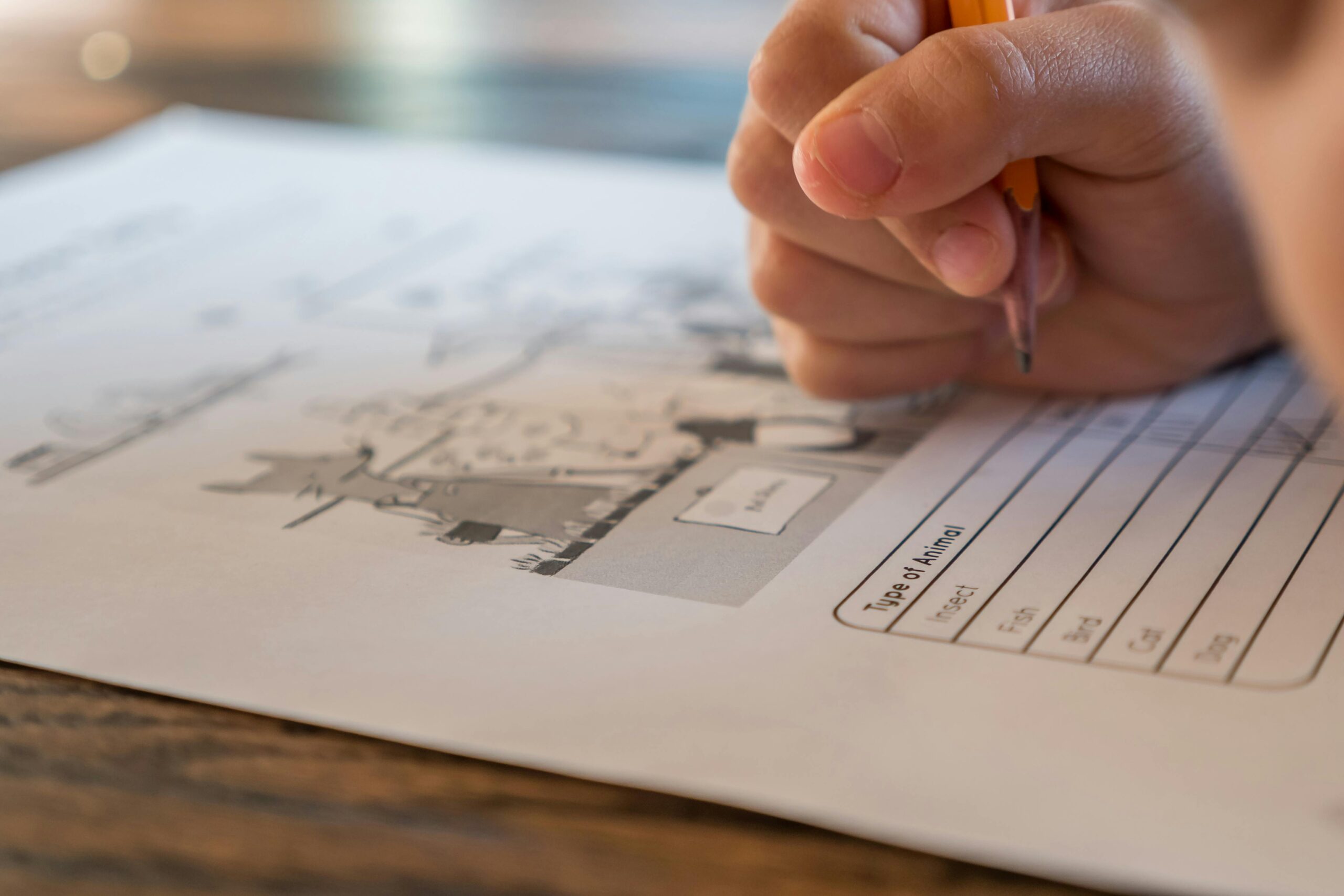 Closeup of crop anonymous elementary school pupil with pencil in hand doing marks on paper sheet with test about animals during lesson