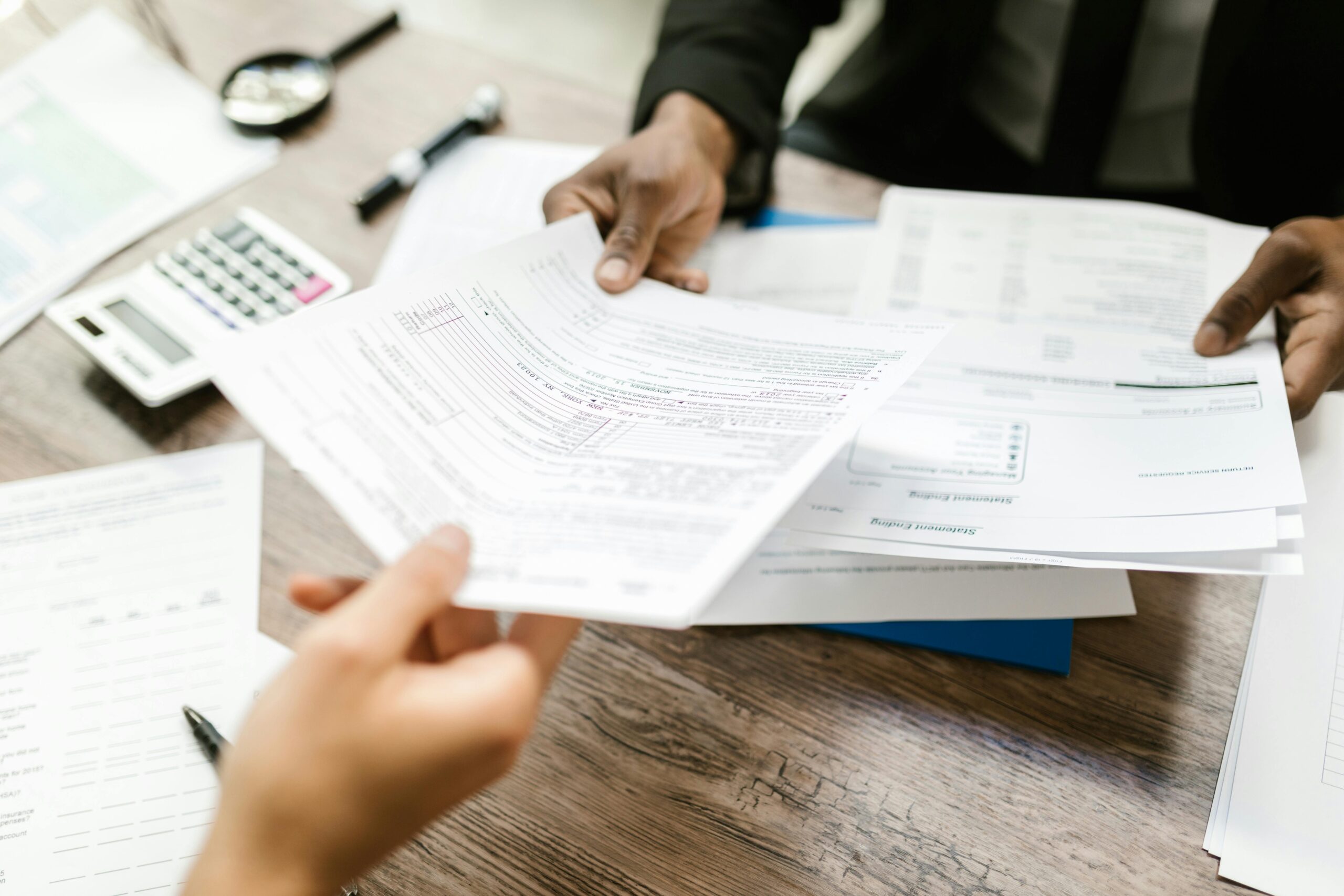 Two professionals exchanging documents in an office setting, focusing on paperwork and data analysis.